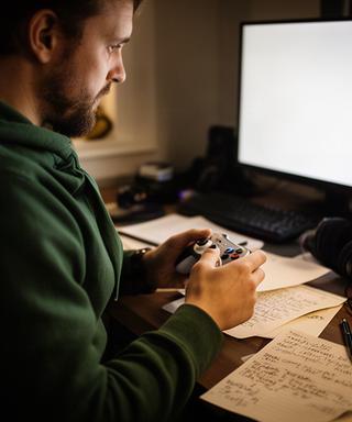 Game critic with a controller at a Pennsylvania review desk covered in handwritten notes
